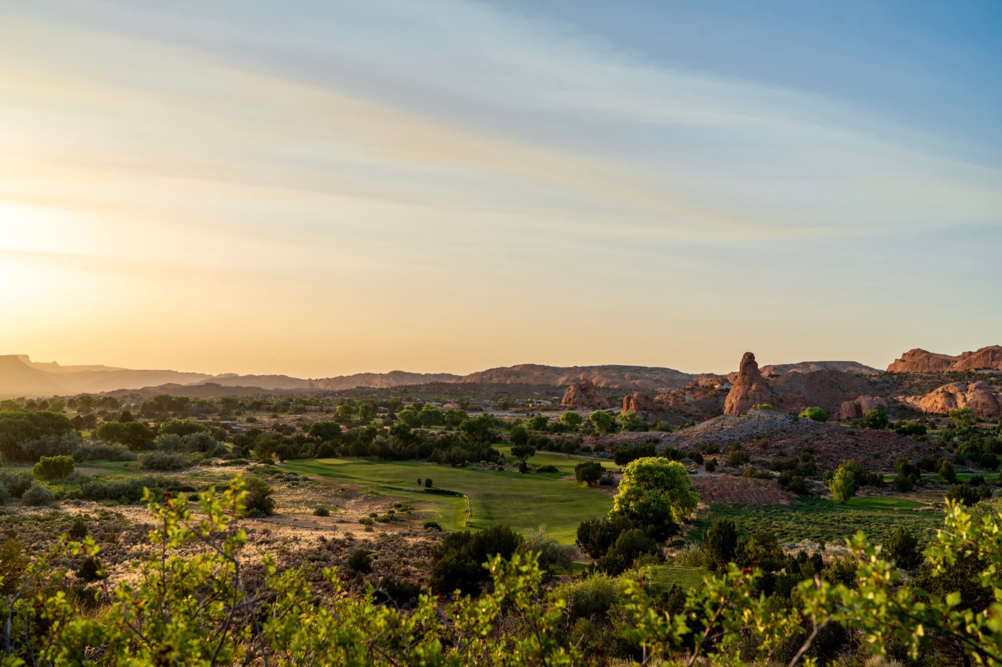 The course spread through Spanish Valley at sunset, red-rock fins and a lone sandstone tower on the skyline